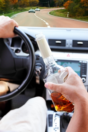 Drunk driver on a forest road with a bottle of alcohol in handの写真素材