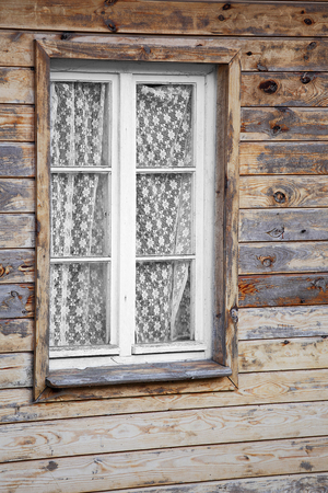 Rural much neglected window in wooden wall of house, wooden backgroundの写真素材