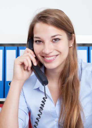 Laughing woman with long blond hair at office talking at phoneの写真素材