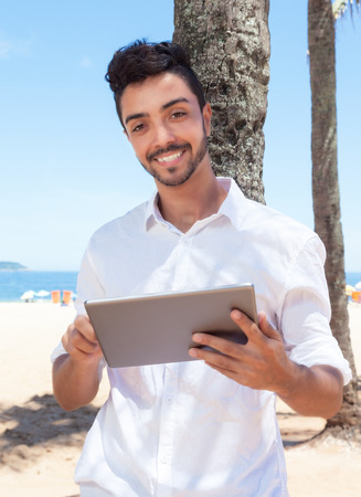 Handsome brazilian guy with tablet at beachの写真素材