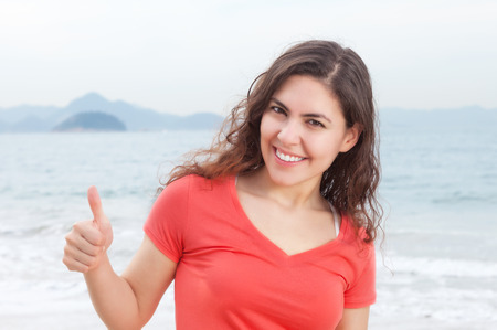 Young woman in a red shirt at beach showing thumbの写真素材