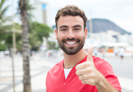 Man with red shirt and beard in the city showing thumbの写真素材