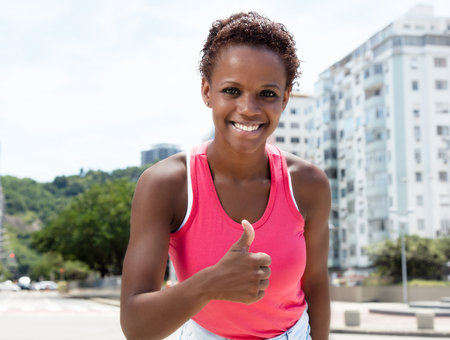 Beautiful african american girl in pink shirt showing thumb in cityの写真素材