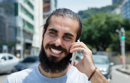 Hipster man with beard laughing at phone in the cityの写真素材