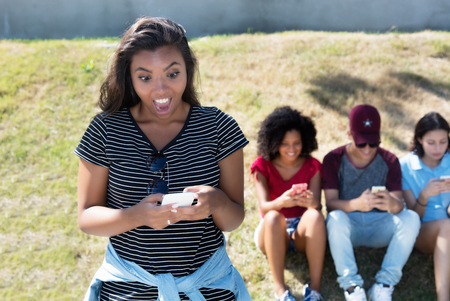 Surprised latin american woman with phone receiving fake news outdoors in summerの写真素材