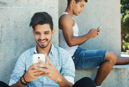 Two happy latin american guys playing a game with phone outdoors in summerの写真素材