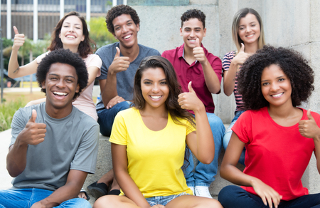 Large group of pretty international young adults showing thumb up outdoors in the summer