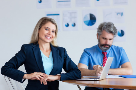 Beautiful german businesswoman with blond hair and computer at desk at office of companyの写真素材