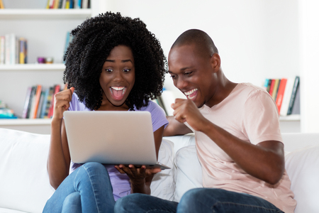 African american couple shopping online with computer indoors at homeの写真素材