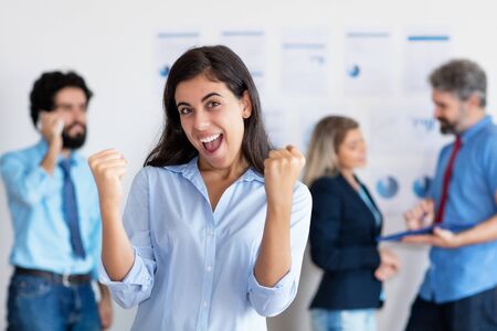 Cheering latin american businesswoman with international team in backgroundの写真素材