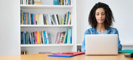 Beautiful latin female student with curly hair at computer with copy spaceの写真素材
