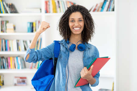 Cheering latin female student with curly hair and paperworkの写真素材