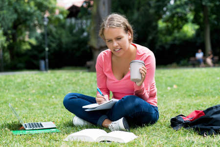 German female student with cup of coffee learning and writing notesの写真素材