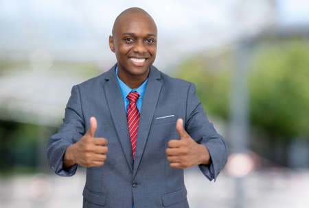 Successful african american businessman showing thumbs up outdoors in the cityの写真素材