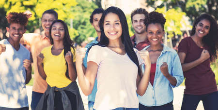 Happy south american female student with group of cheering young adultsの写真素材