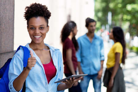 Laughing african american female student with tablet computer and group of young adultsの写真素材
