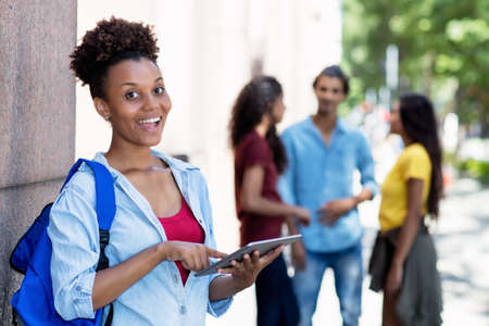 Beautiful african american female student with tablet computer and group of young adultsの写真素材