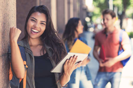 Cheering latin american female student with digital tablet computer and other young adultsの写真素材