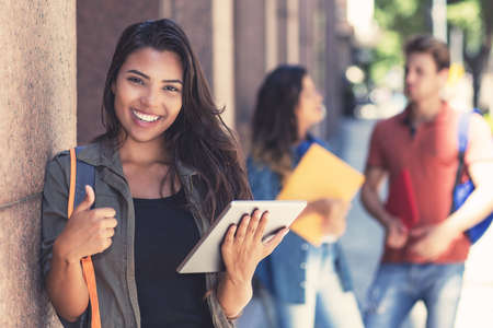 Successful latin american female student with digital tablet computer and other young adultsの写真素材