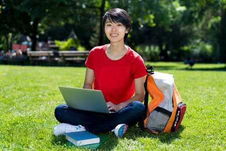 Laughing east asian male student learning at computer at campus of universityの写真素材