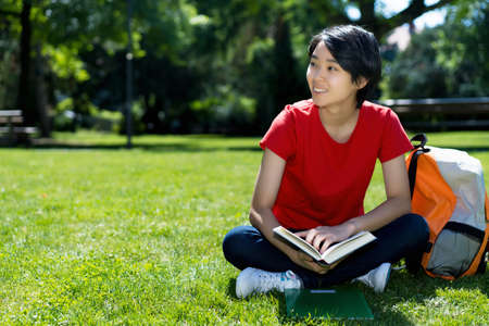 Laughing east asian male student learning with book on campus of universityの写真素材