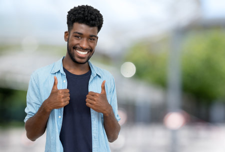 Cheering young adult man from Africa with beard and casual clothes outdoor in city in summerの写真素材