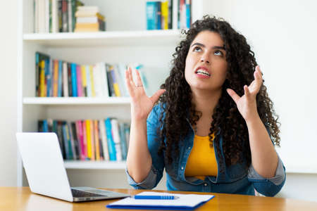 Angry hispanic woman hates quarantine and working indoors at home at computer during the pandemicの写真素材
