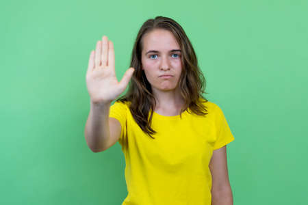 Young woman with brunette hair gesturing stop and distance isolated on green backgroundの写真素材