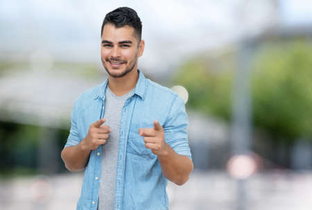 Laughing hispanic hipster man with beard and casual clothes outdoor in summer in city