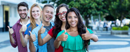Group of five laughing international young adults in line showing thumbs up