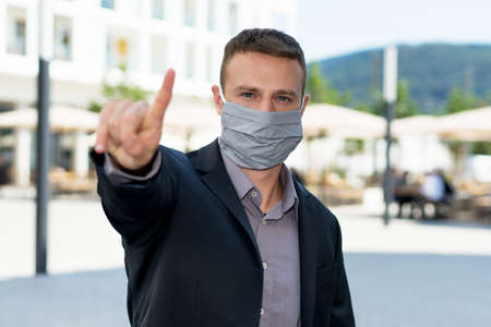 Businessman man with face mask as protection against corona virus infection gesturing stop outdoor...