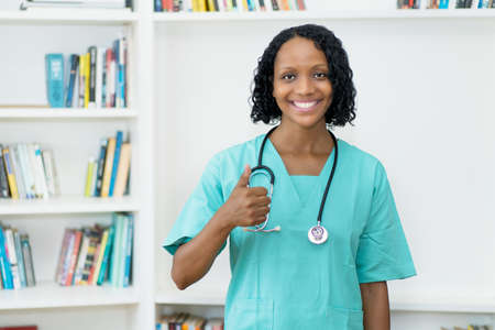 Laughing african american mature nurse showing thumb up at clinicの写真素材