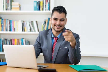 Laughing mexican businessman at computer indoors at officeの写真素材