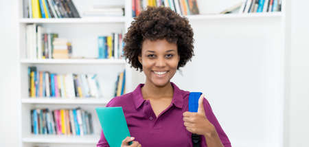 Successful afro american female student with backpack and paperwork at classroom of universityの写真素材