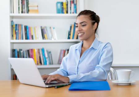 Beautiful latin american business trainee working at computer at desk at officeの写真素材