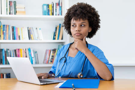 Concerned afro american nurse or medical student at computer at hospitalの写真素材