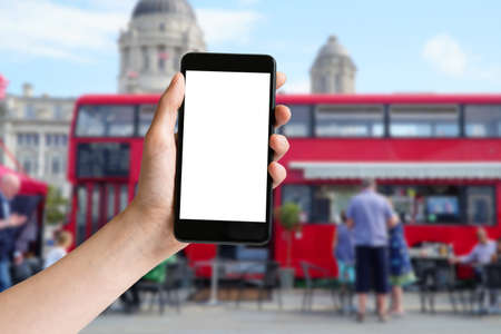 Hand holding mobile phone with blank screen and red bus at London
