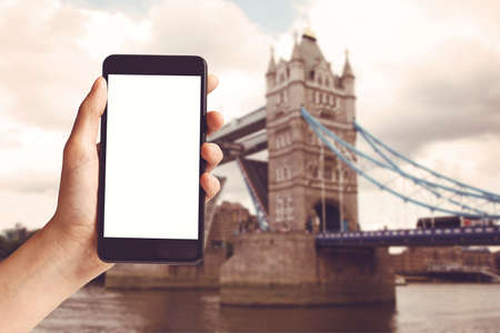 Hand holding mobile phone with blank screen and London Tower Bridge at United Kingdomの写真素材
