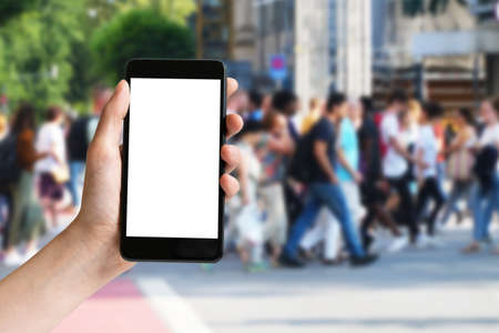 Hand holding mobile phone with blank screen and group of people in city in summerの写真素材