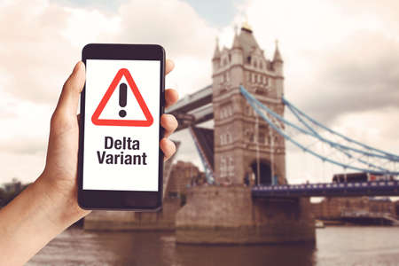 Hand holding mobile phone with with warning message delta variant and London Tower Bridge ar United Kingdomの写真素材