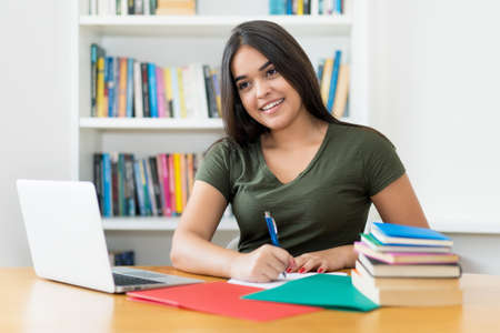 Pretty spanish female student learning at desk indoors at libraryの写真素材