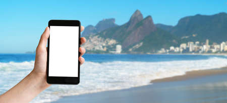 Banner - Hand holding mobile phone with blank screen at Ipanema beach at Rio de Janeiroの写真素材