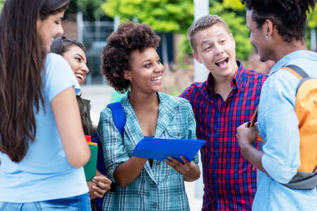 Pretty african american exchange student talking with latin and hispanic young adults outdoor in summer in cityの写真素材