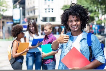 Optimistic mexican male student with other young adults outdoor in summer in cityの写真素材