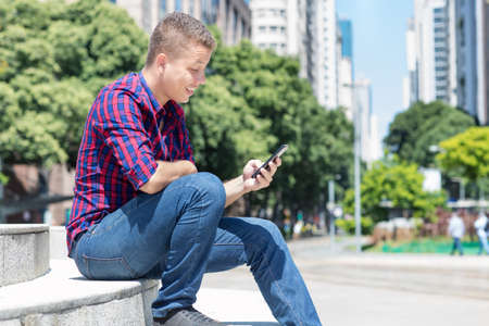 German young adult man playing online game with mobile phone outdoor in city in summerの写真素材