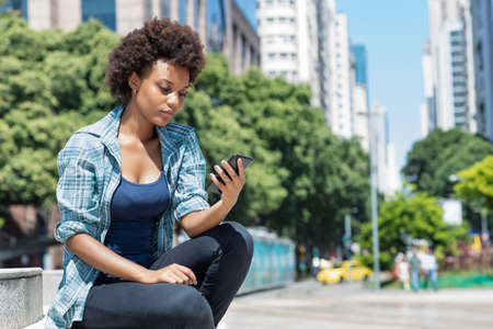 African american young adult woman watching video clip with mobile phone outdoor in city in summerの写真素材