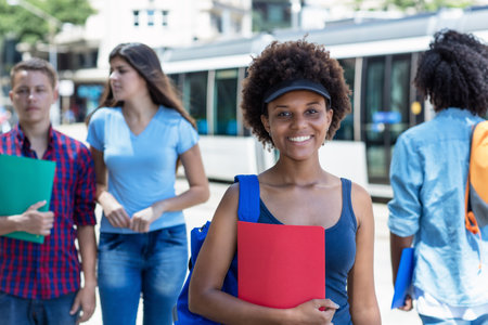 Laughing african american female student walking to university outdoor in summer in cityの写真素材
