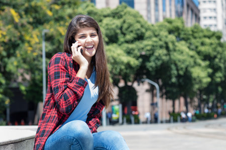 Beautiful spanish woman at phone outdoor in city in summerの写真素材