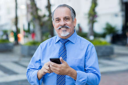 Handsome latin american senior businessman shopping online with phone outdoor in city in summerの写真素材