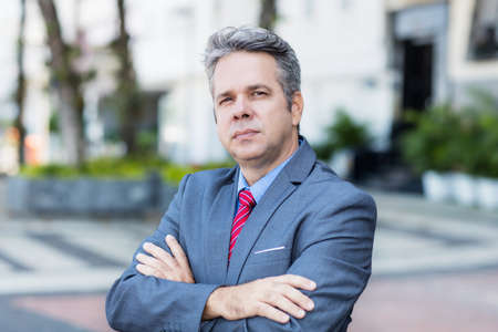 Portrait of serious mature businessman with suit and gray hair outdoor in city in summerの写真素材